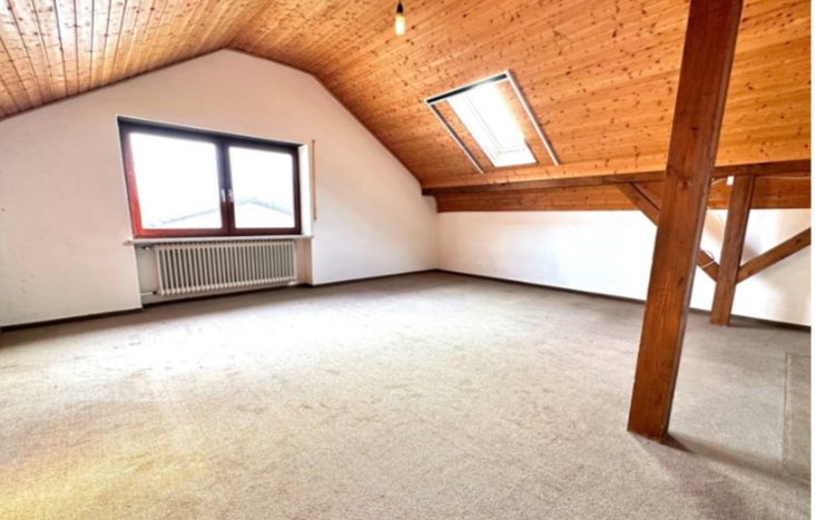 Ungedämmter Dachboden mit Holzbalken, altem Teppichboden und unverkleideter Schräge