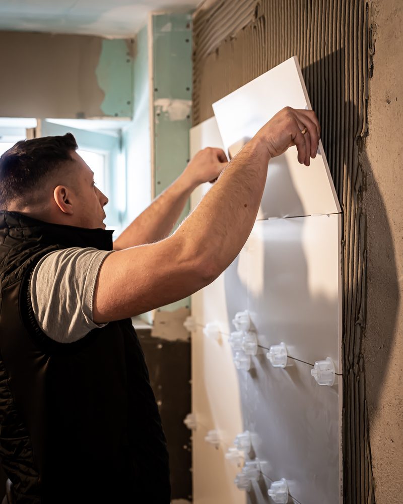 Handwerker setzt eine großformatige Wandfliese im Badezimmer