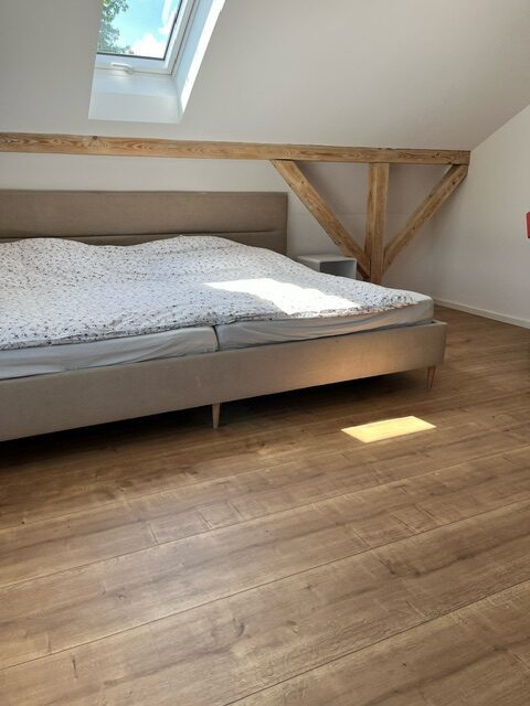 Schlafzimmer im ausgebauten Dachgeschoss mit sichtbarem Holzbalken und Dielenboden